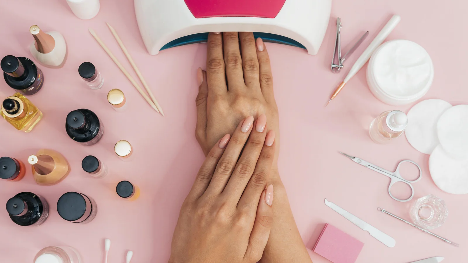 Flat lay of nail salon tools, gel polish bottles and a UV lamp around a client's hands